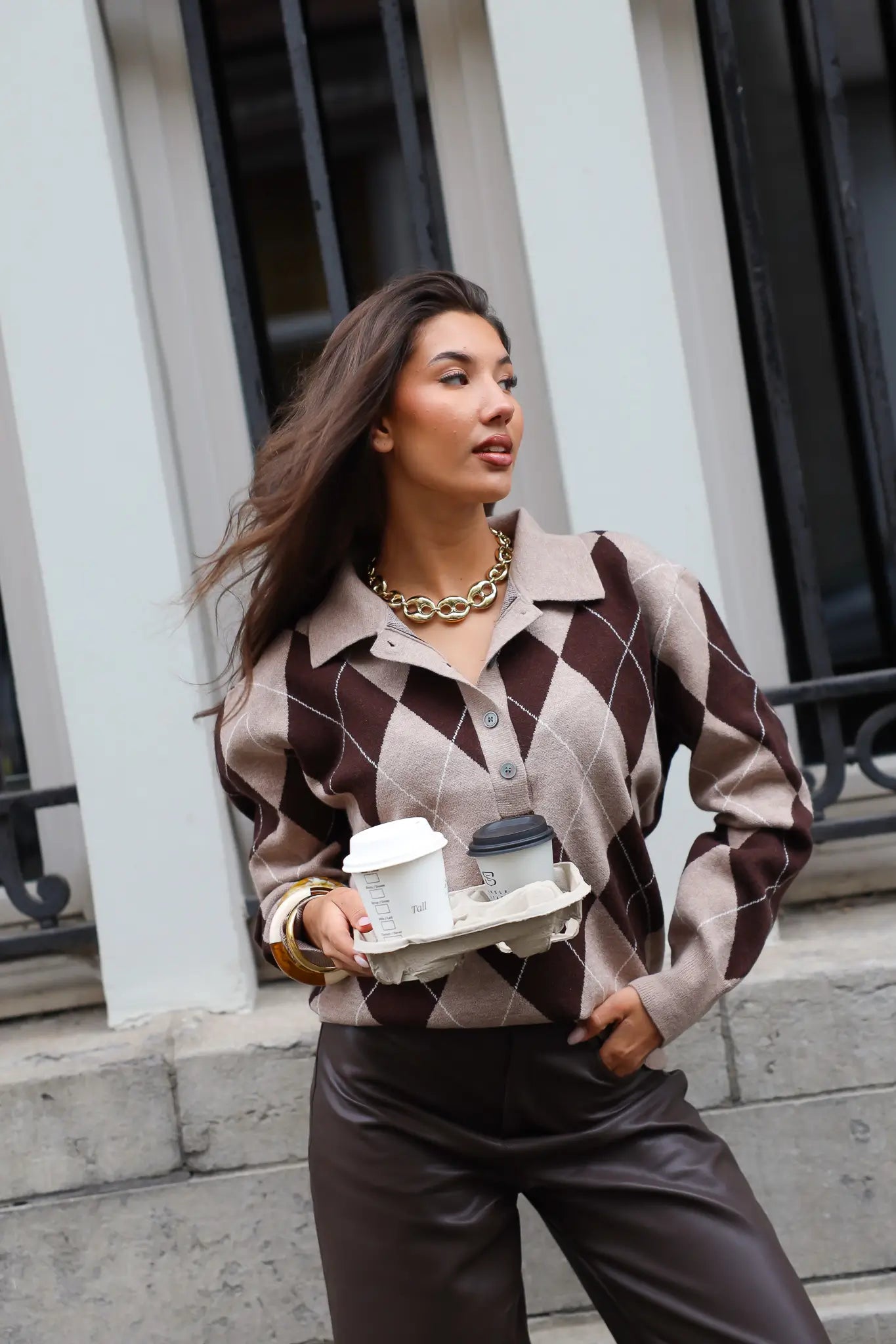 Model met argyle trui bruin beige, houdend koffiebeker buiten