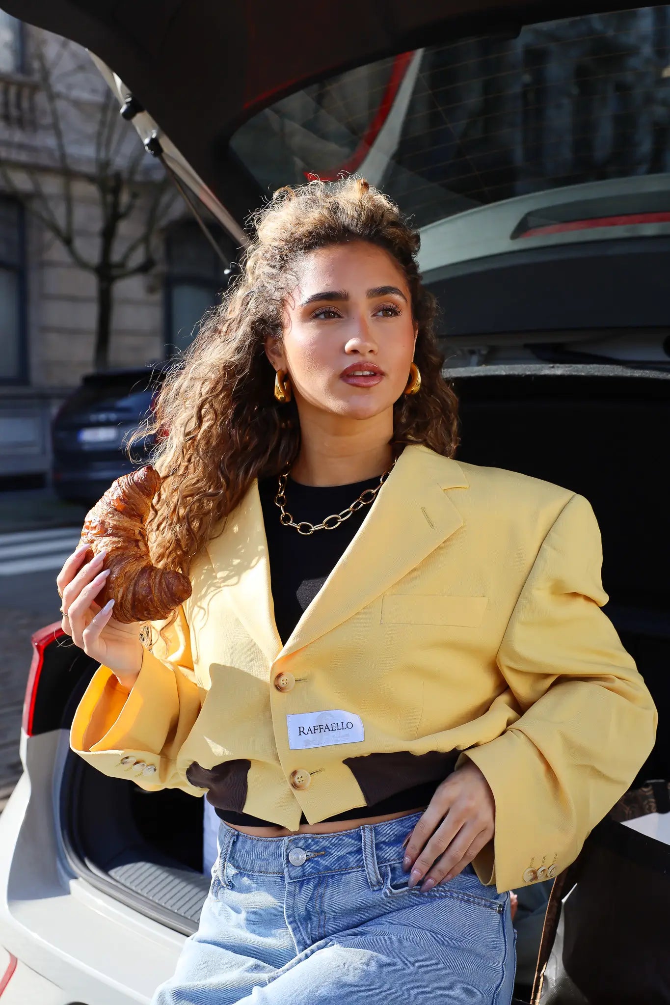 model draagt atelier series reworked blazer cropped geel bij open auto kofferbak