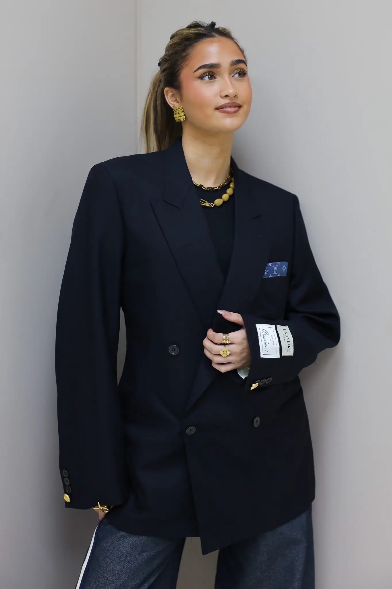 Model draagt donkerblauwe double breasted blazer met goudkleurige knopen en borstzak