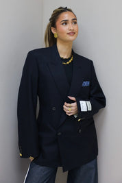 Model draagt donkerblauwe double breasted blazer met goudkleurige knopen en borstzak