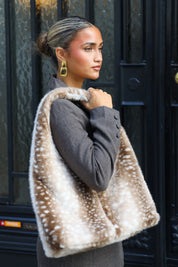 Close-up van een beige Bambi schoudertas met zachte bontlook en bruine hertenprint bij een grijze blazer