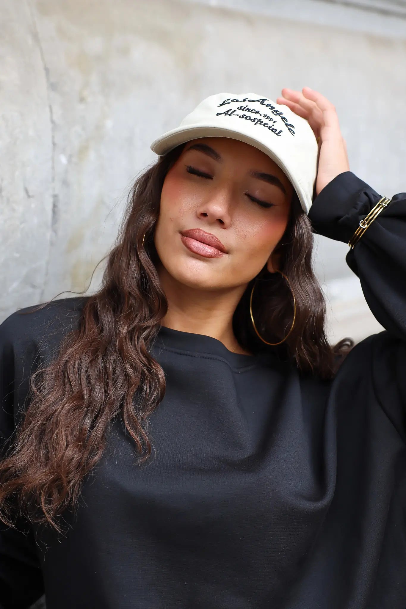Close-up van beige baseball pet met zwart borduursel en gebogen klep gedragen met zwarte kleding
