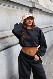 Beige baseball pet voor dames gedragen met zwarte cropped sweater en wijde zwarte broek