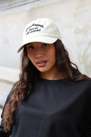 Close-up van beige Los Angeles pet met zwarte geborduurde letters gedragen bij een zwarte sweater