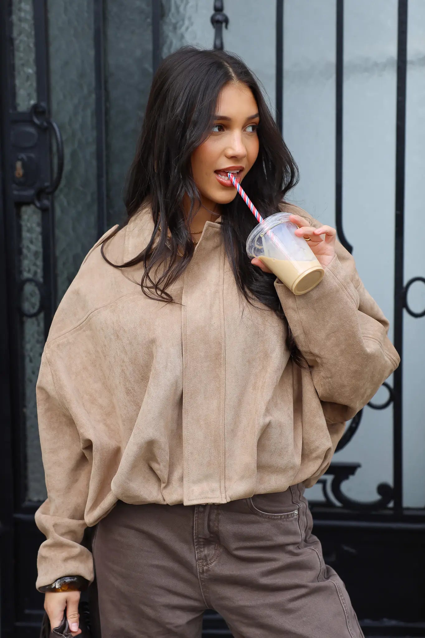 Model draagt een beige suede blouse voor een zwarte deur