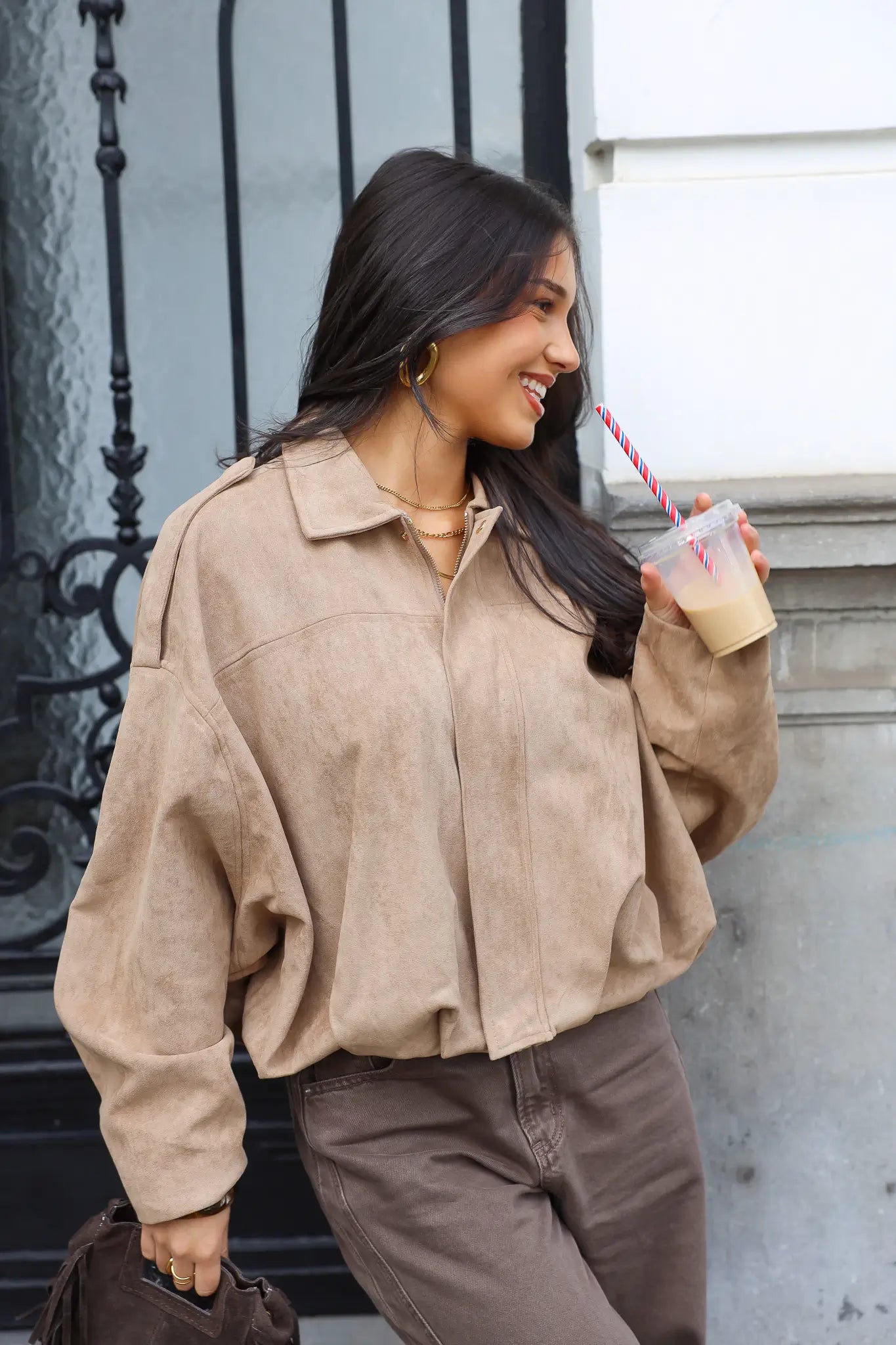 Model drinkt een drankje terwijl ze een beige suede blouse draagt