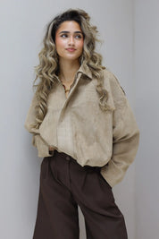 Model poseert tegen een muur met beige suede blouse