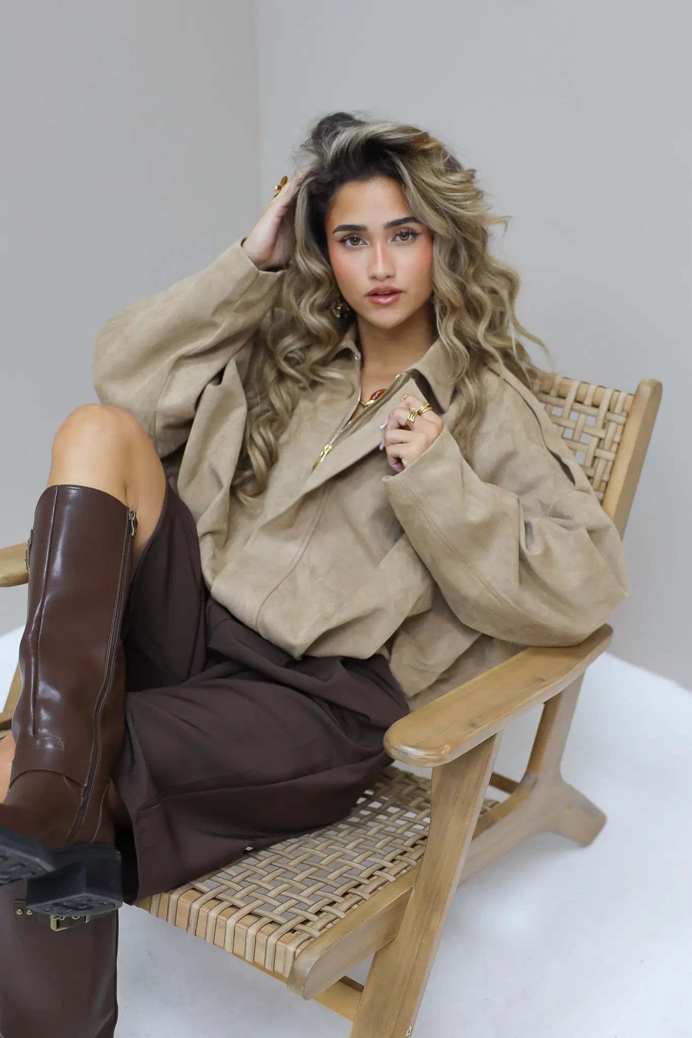 Model zit op een houten stoel met beige suede blouse en laarzen