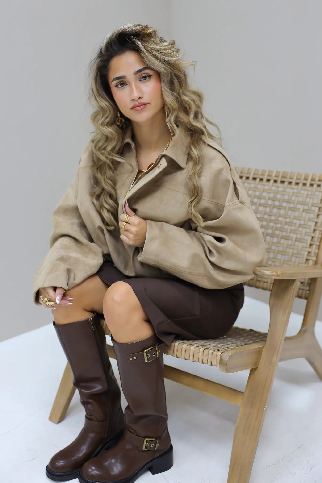Model zit in studio met beige suede blouse en bruine broek