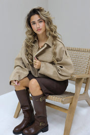 Model zit in studio met beige suede blouse en bruine broek