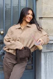 Model loopt met tas terwijl ze een beige suede blouse draagt