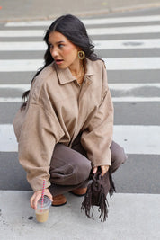 Model zit op de stoep met een beige suede blouse