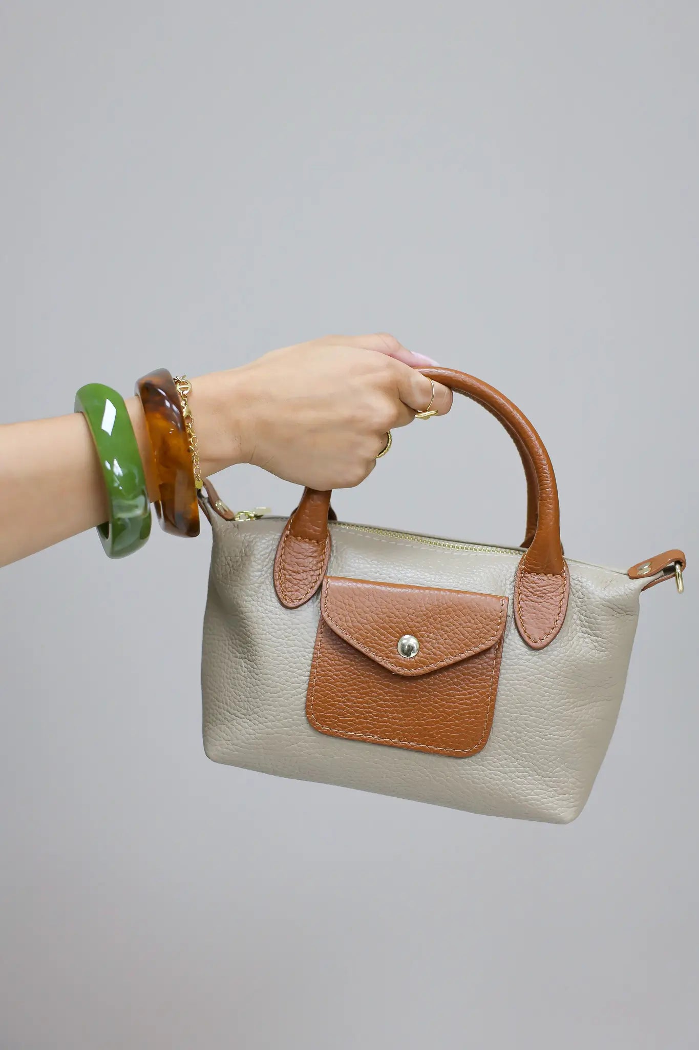 beige handtas met bruine hengsels vastgehouden in de hand voor lichte achtergrond