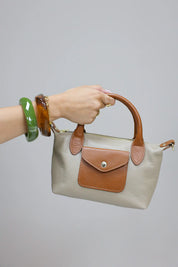 beige handtas met bruine hengsels vastgehouden in de hand voor lichte achtergrond