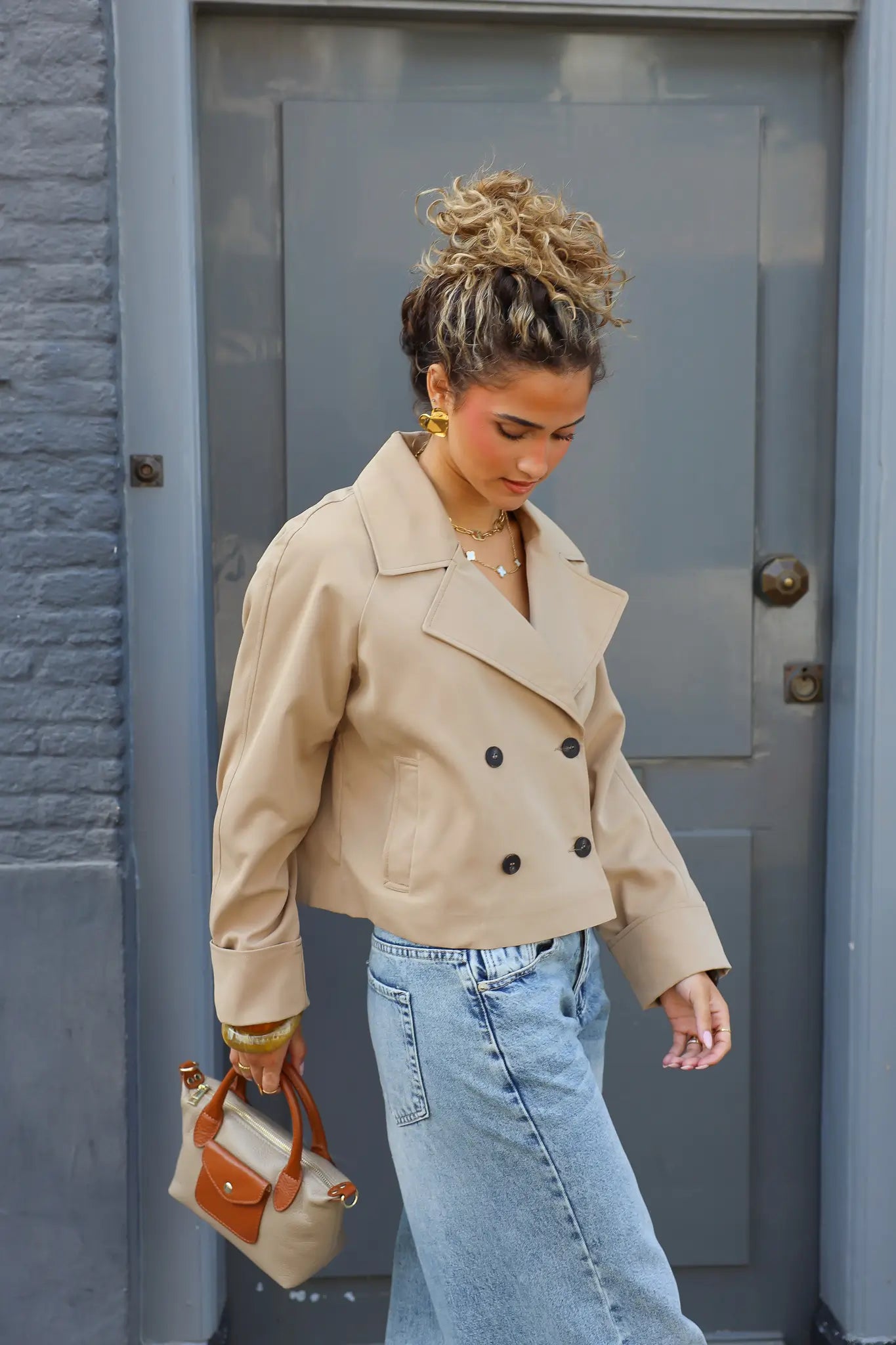 beige handtas met bruine details gedragen bij een beige cropped jas en jeans buiten