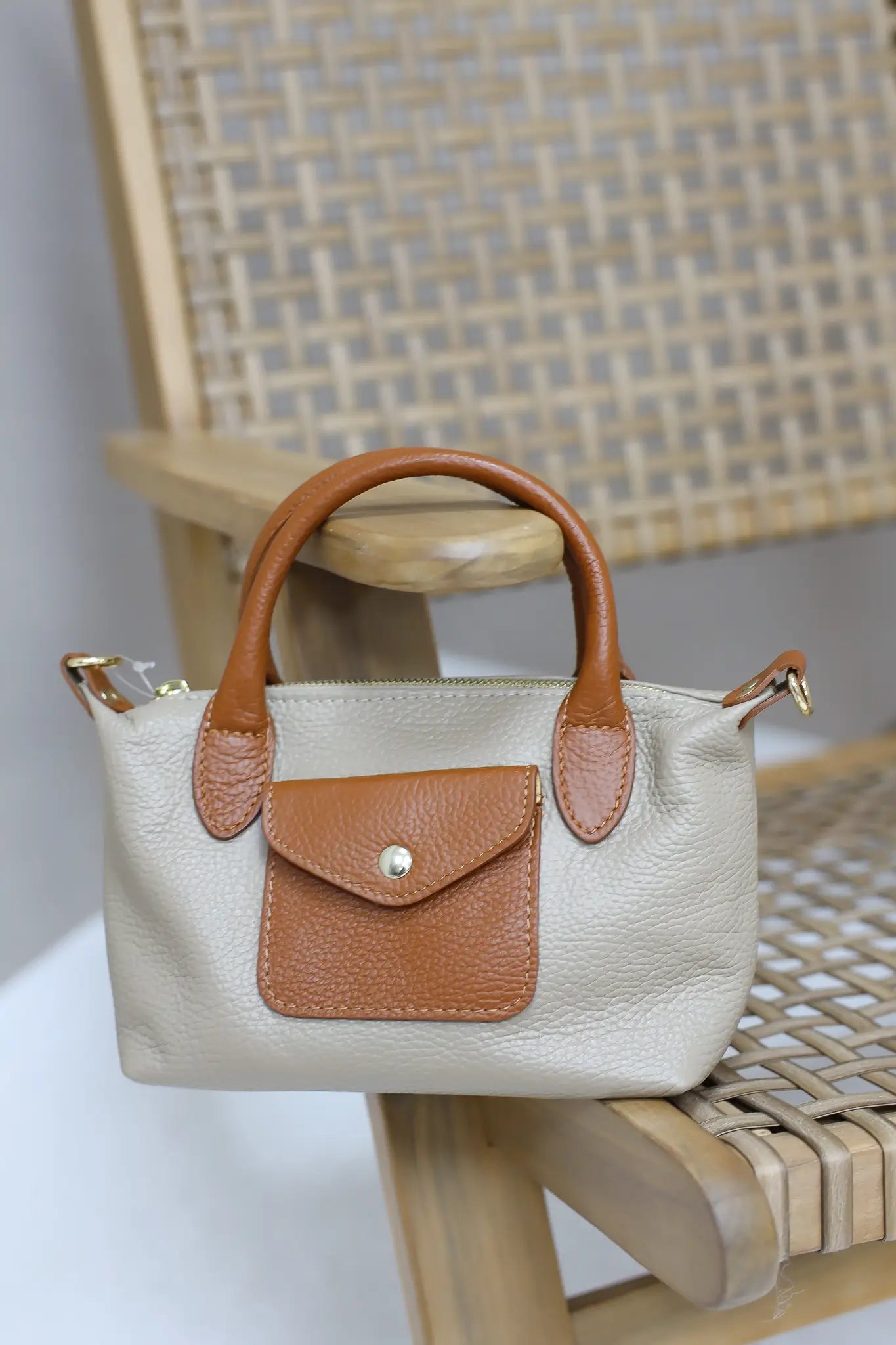 beige handtas met bruine leren klep en hengsels op een houten stoel