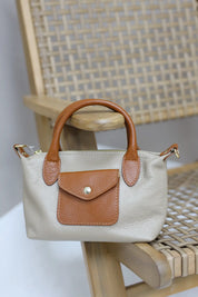 beige handtas met bruine leren klep en hengsels op een houten stoel