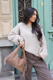 Model draagt beige trui met bruine broek en tas buiten bij groene deur