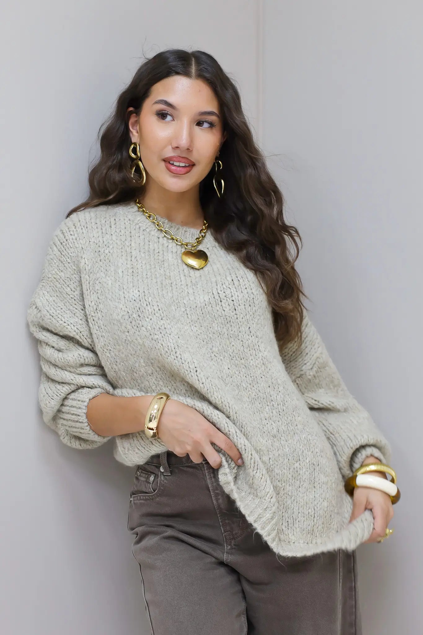 Model poseert in beige trui met bruine broek en gouden sieraden