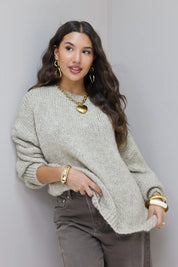 Model poseert in beige trui met bruine broek en gouden sieraden