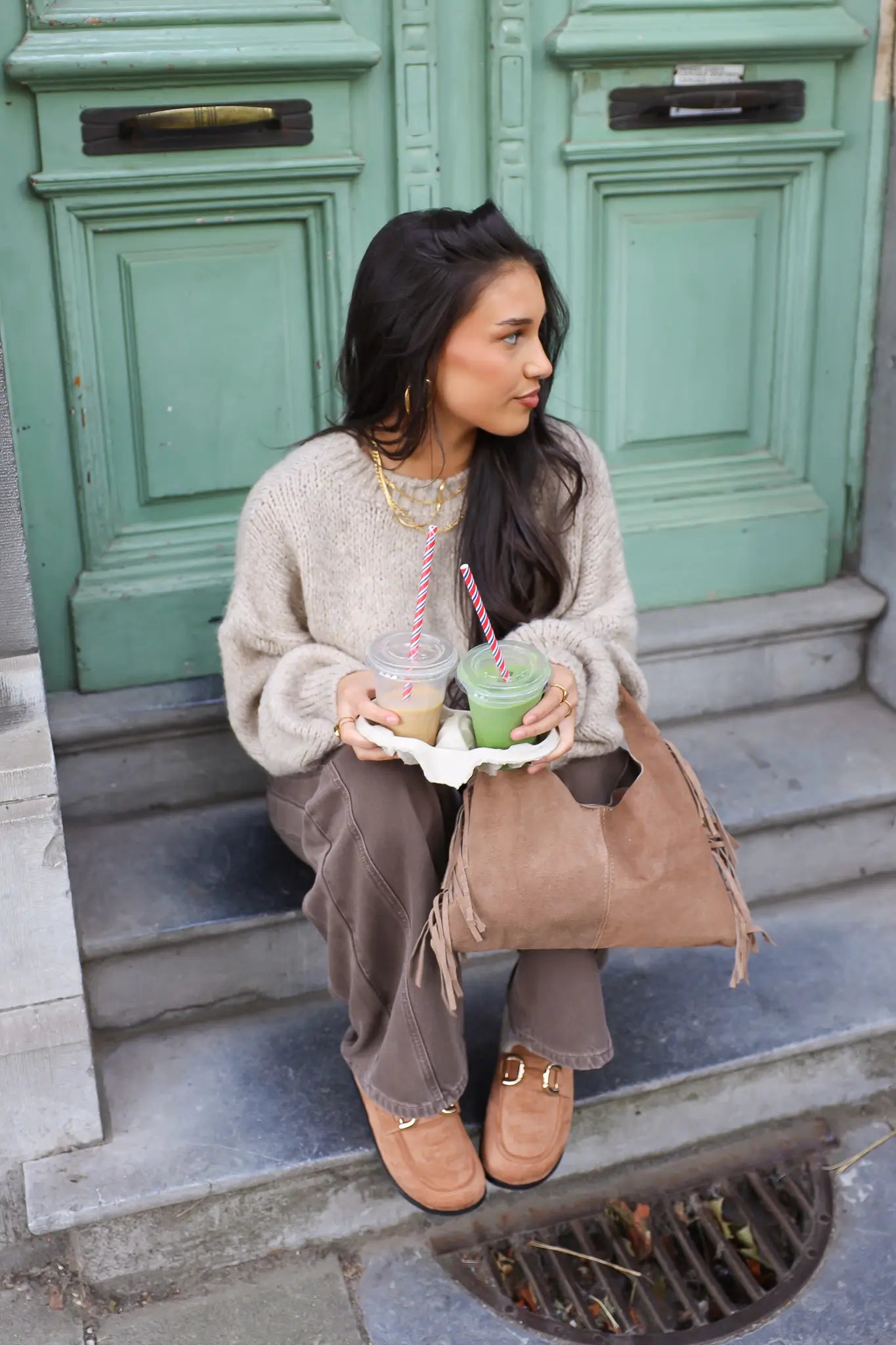 Model zit op traptreden met beige trui en bruine broek en leest tijdschrift