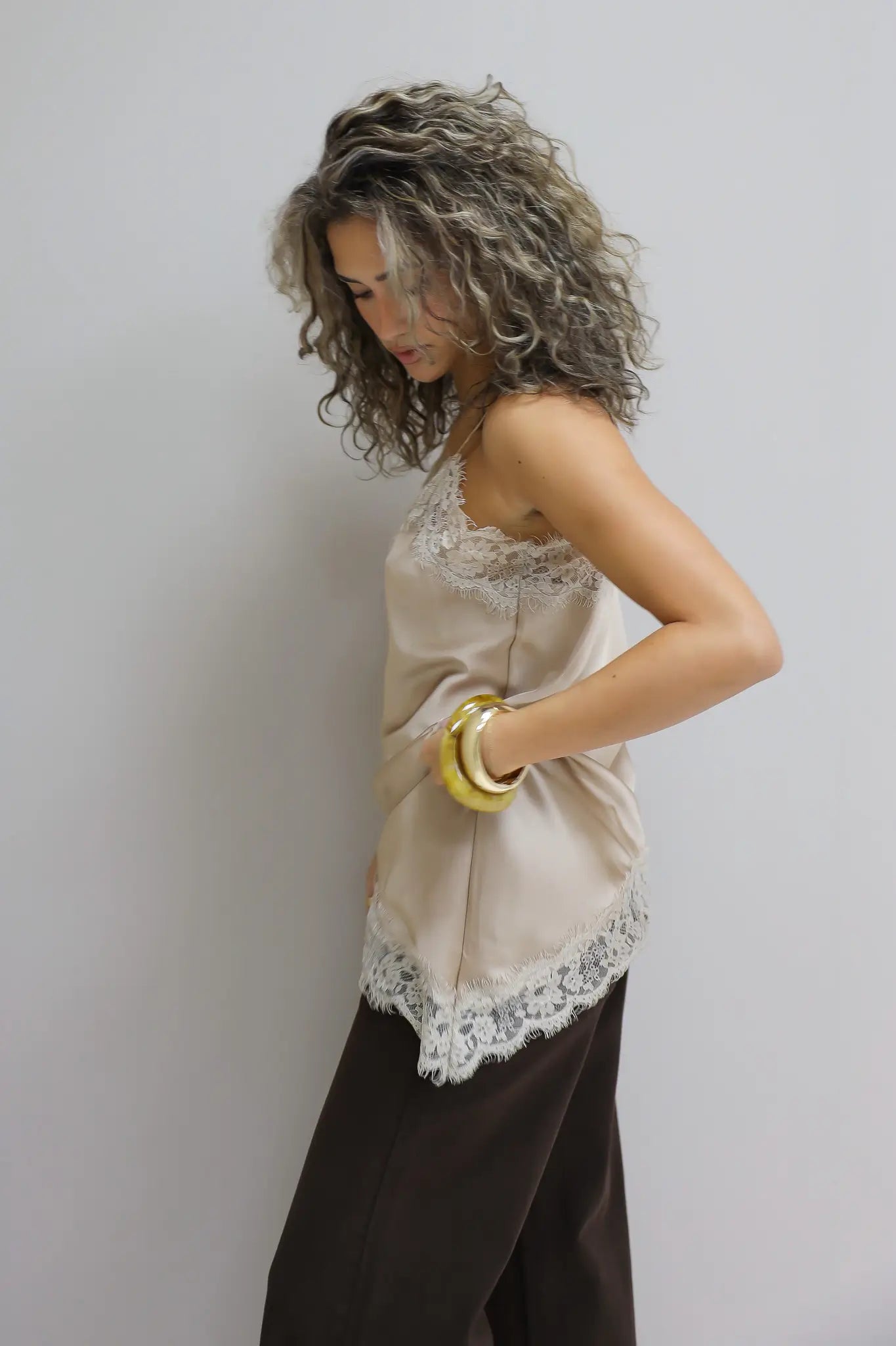 model met beige trui in nonchalante pose tegen lichte muur