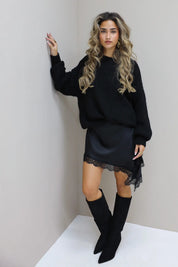 Zwarte satijnen jurk met trui en hoge laarzen in de studio