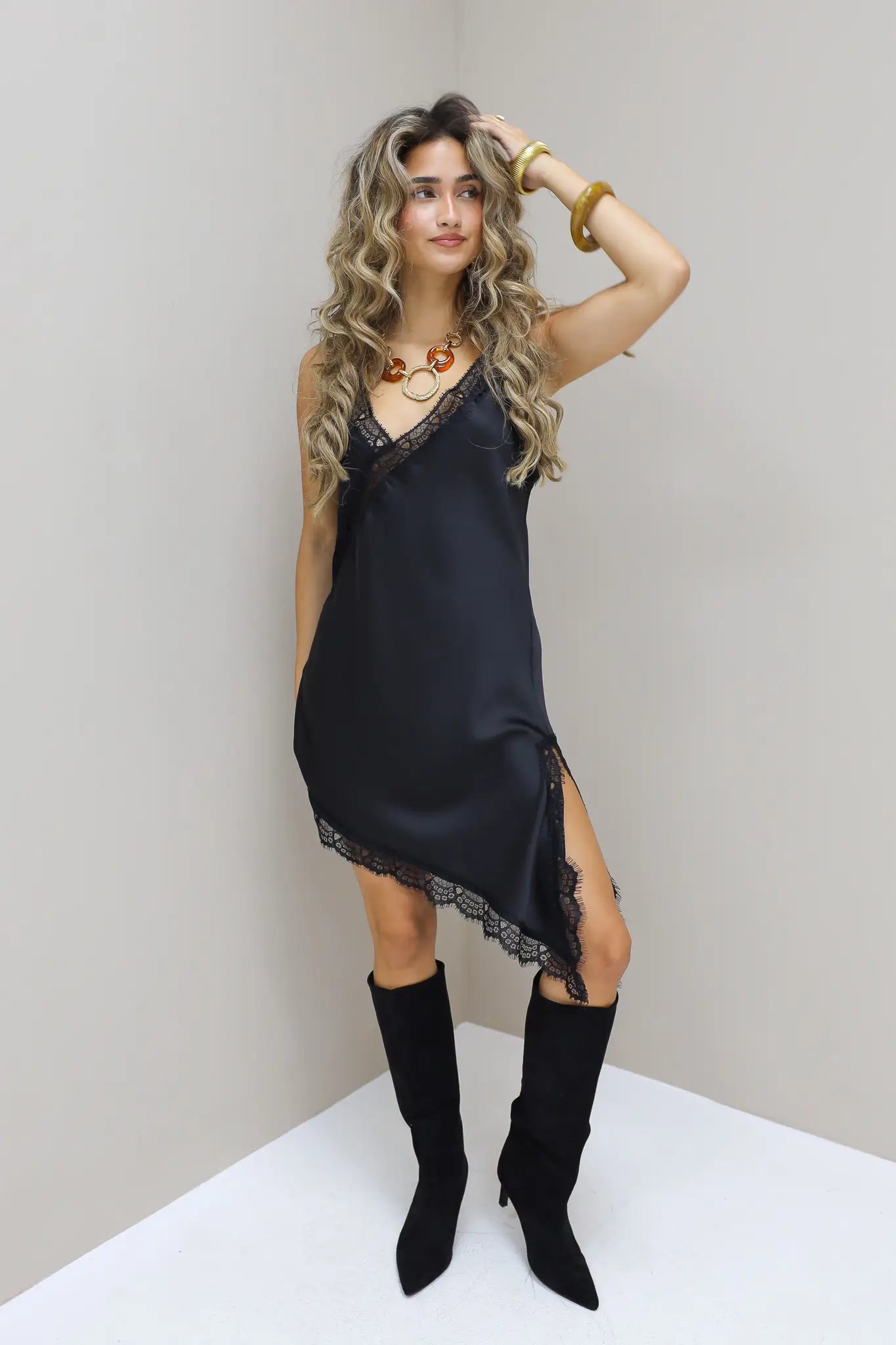 Zwarte satijnen jurk met split en laarzen recht vooruit gefotografeerd