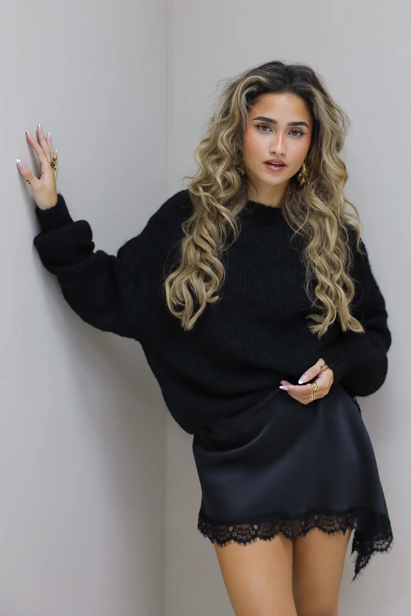 Zwarte trui met satijnen onderjurk, hand in zij in de studio