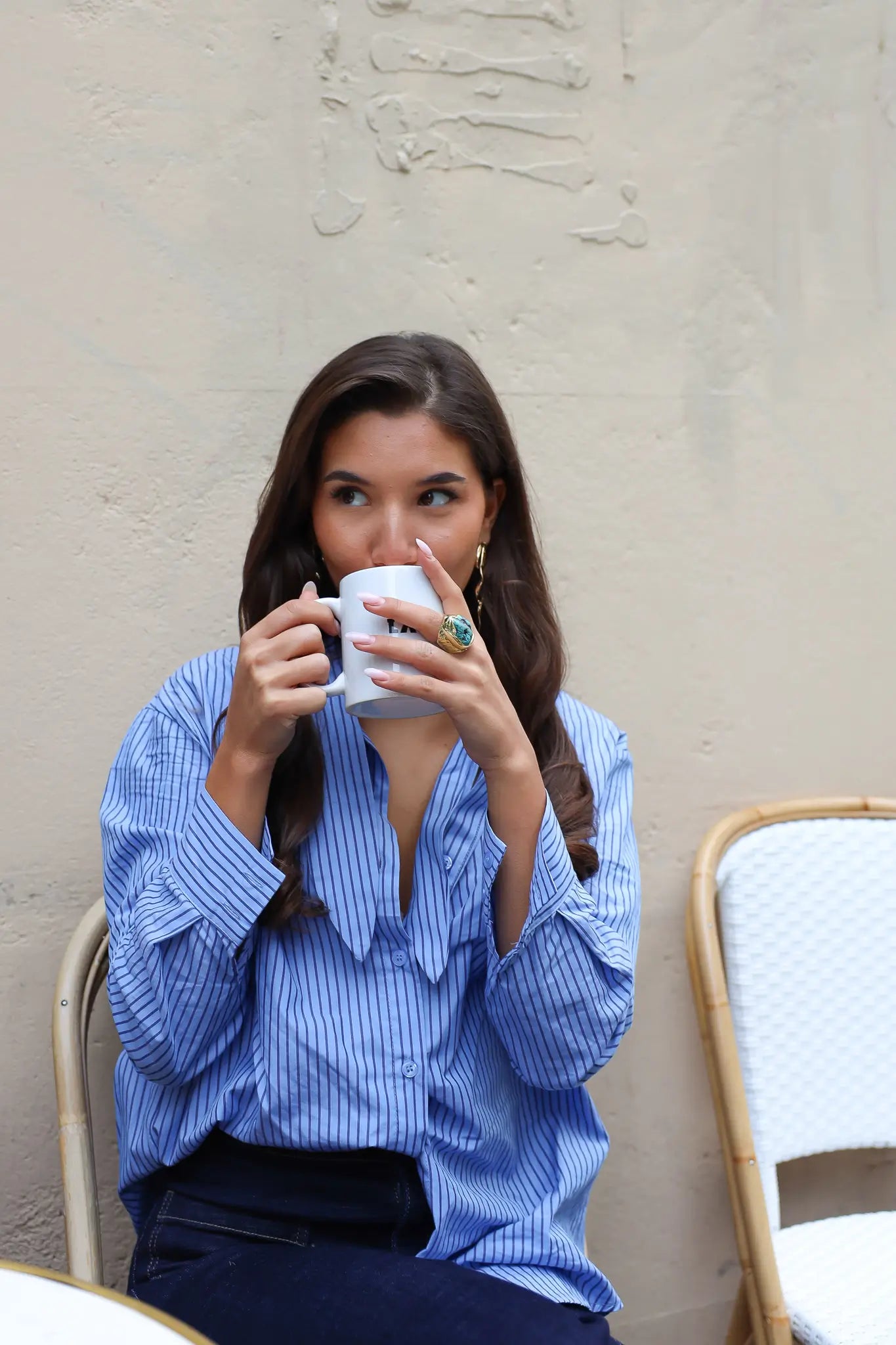 blauwe gestreepte blouse model recht van voren zittend met kop koffie