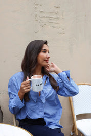blauwe gestreepte blouse model zittend in zijaanzicht met koffie