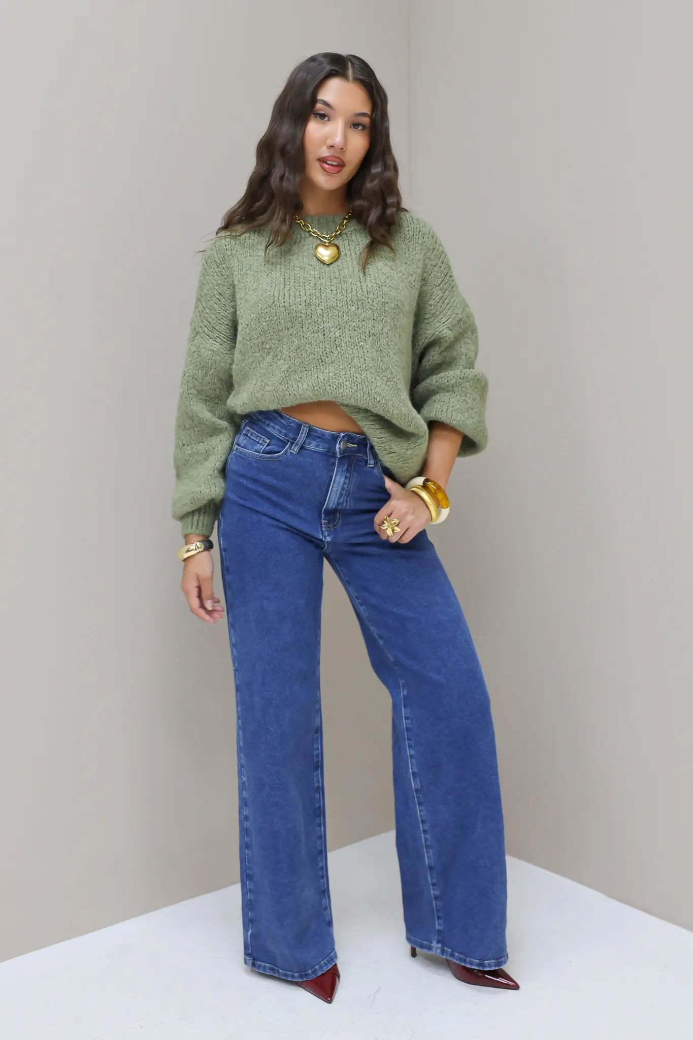 Model kijkt recht vooruit in blauwe wijde jeans met groene trui