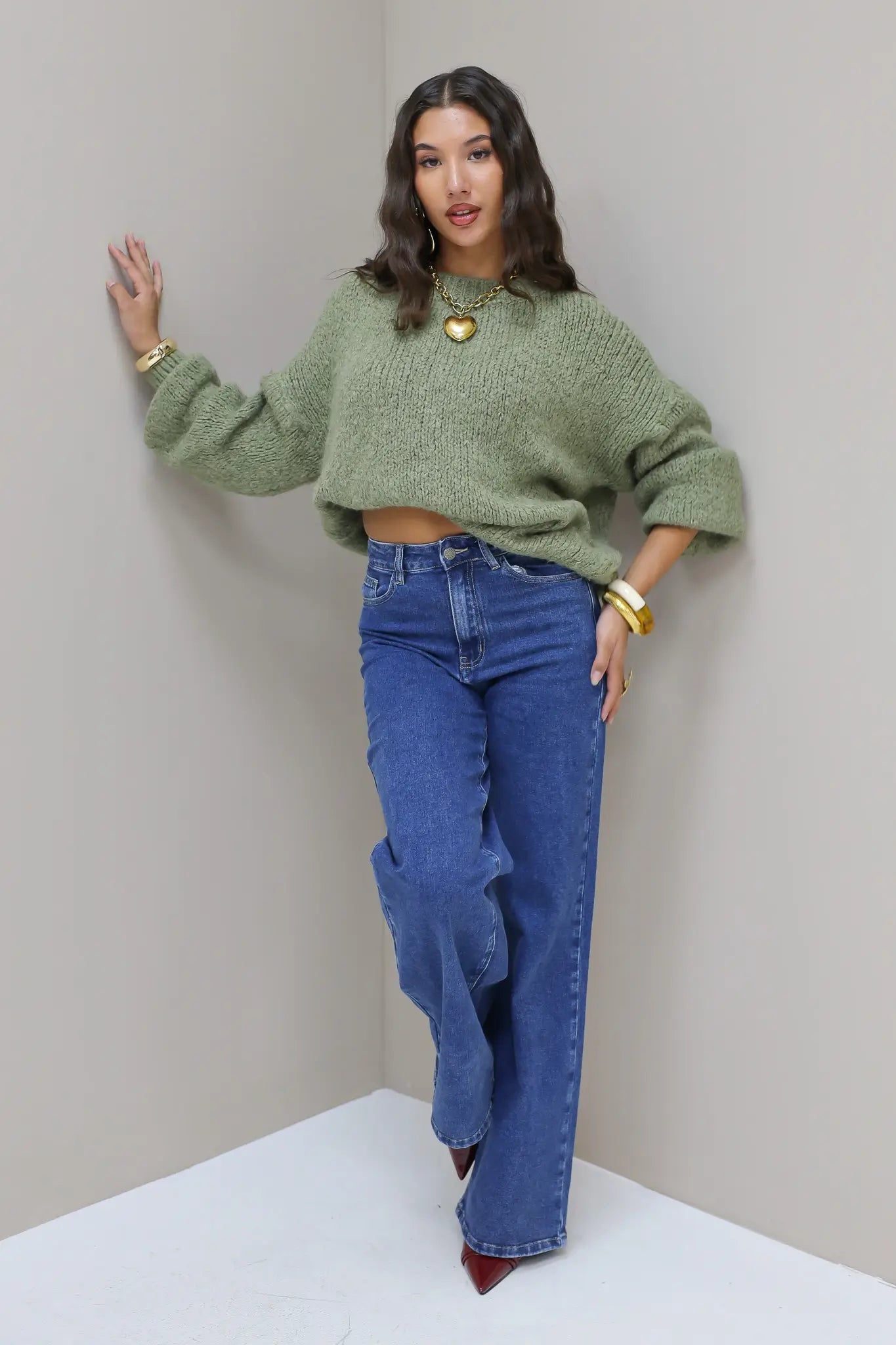 Model leunt licht tegen muur in blauwe wijde jeans met groene trui
