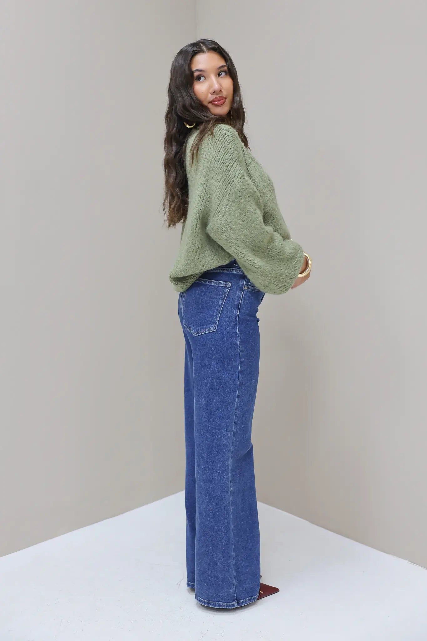 Model in zijaanzicht met blauwe wijde jeans en groene trui