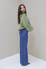 Model in zijaanzicht met blauwe wijde jeans en groene trui