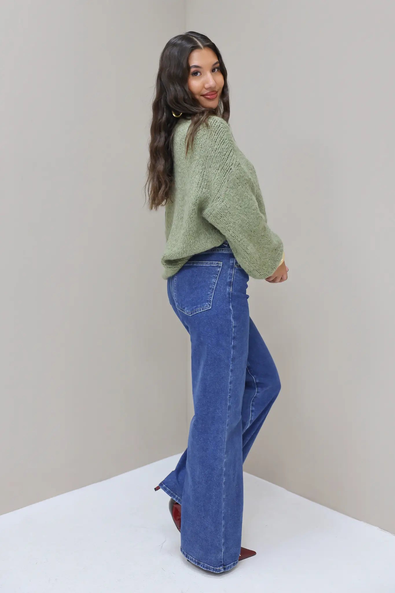 Model poseert zijwaarts in blauwe wijde jeans met groene trui