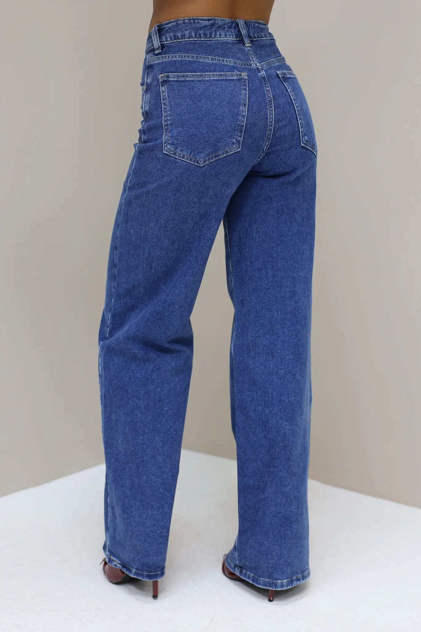 Schuin achteraanzicht van blauwe wijde jeans met lichte wassing en hakken