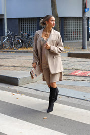 vrouw met beige oversized blazer en matching short draagt hoge laarzen op straat