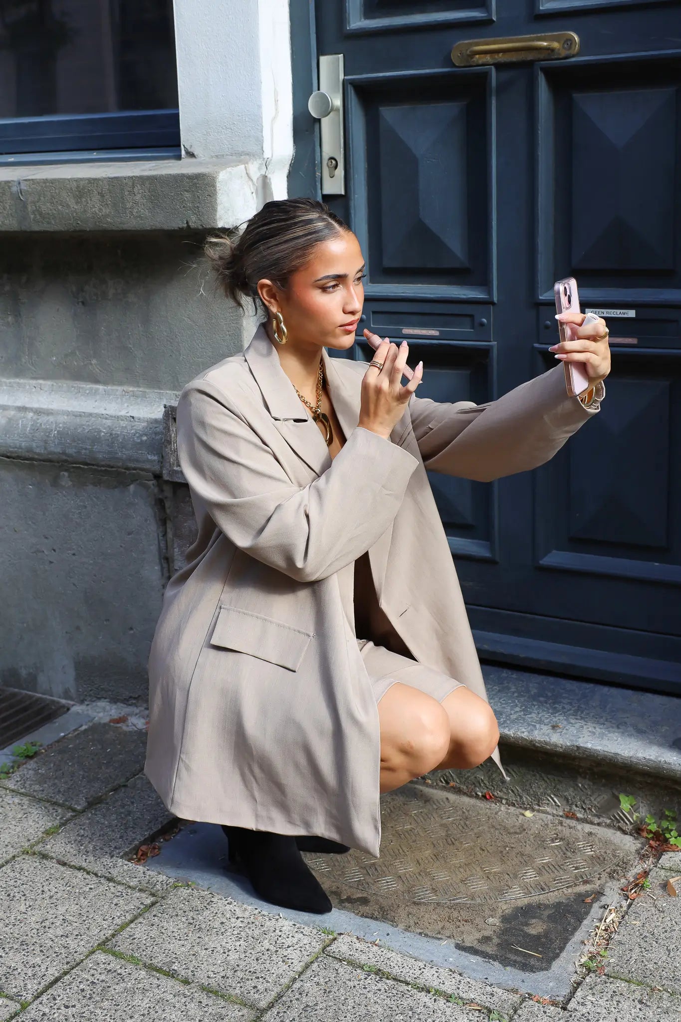 vrouw met beige oversized blazer en zwarte laarzen hurkt en kijkt opzij