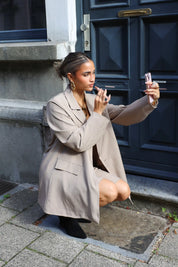 vrouw met beige oversized blazer en zwarte laarzen hurkt en kijkt opzij