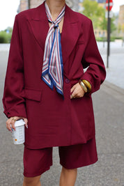 close up van vrouw met bordeaux oversized blazer en geknoopte sjaal bij ingang van gebouw