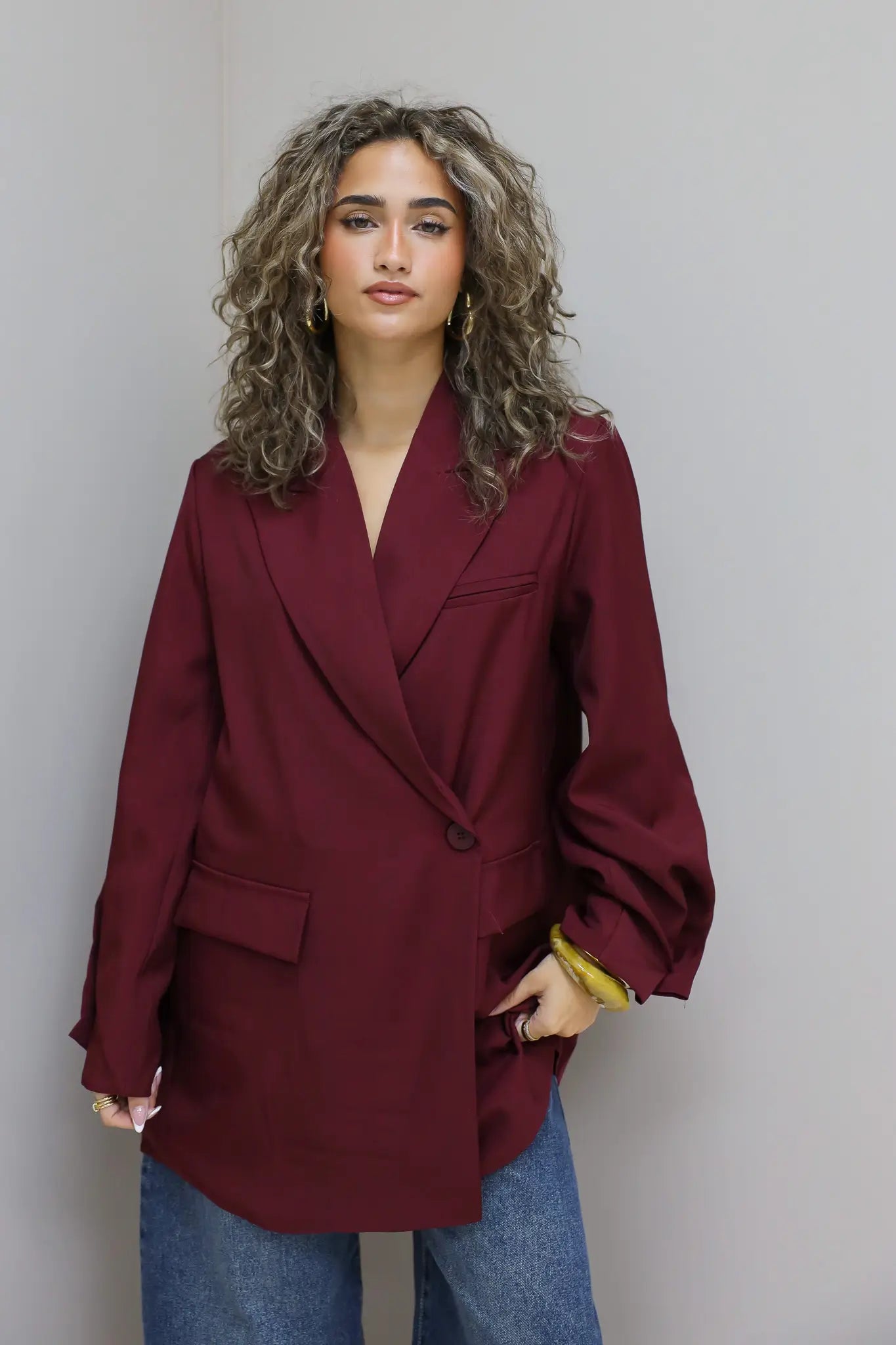 vrouw kijkt recht vooruit met handen in zakken terwijl ze bordeaux oversized blazer draagt