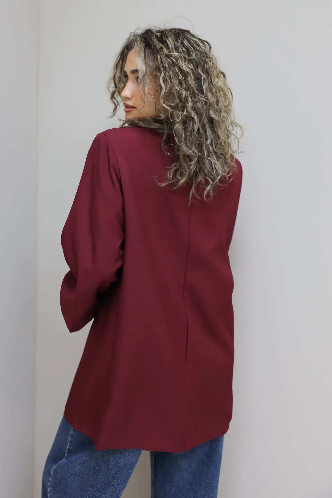 zijaanzicht van vrouw met krullen in bordeaux oversized blazer met lichte voering