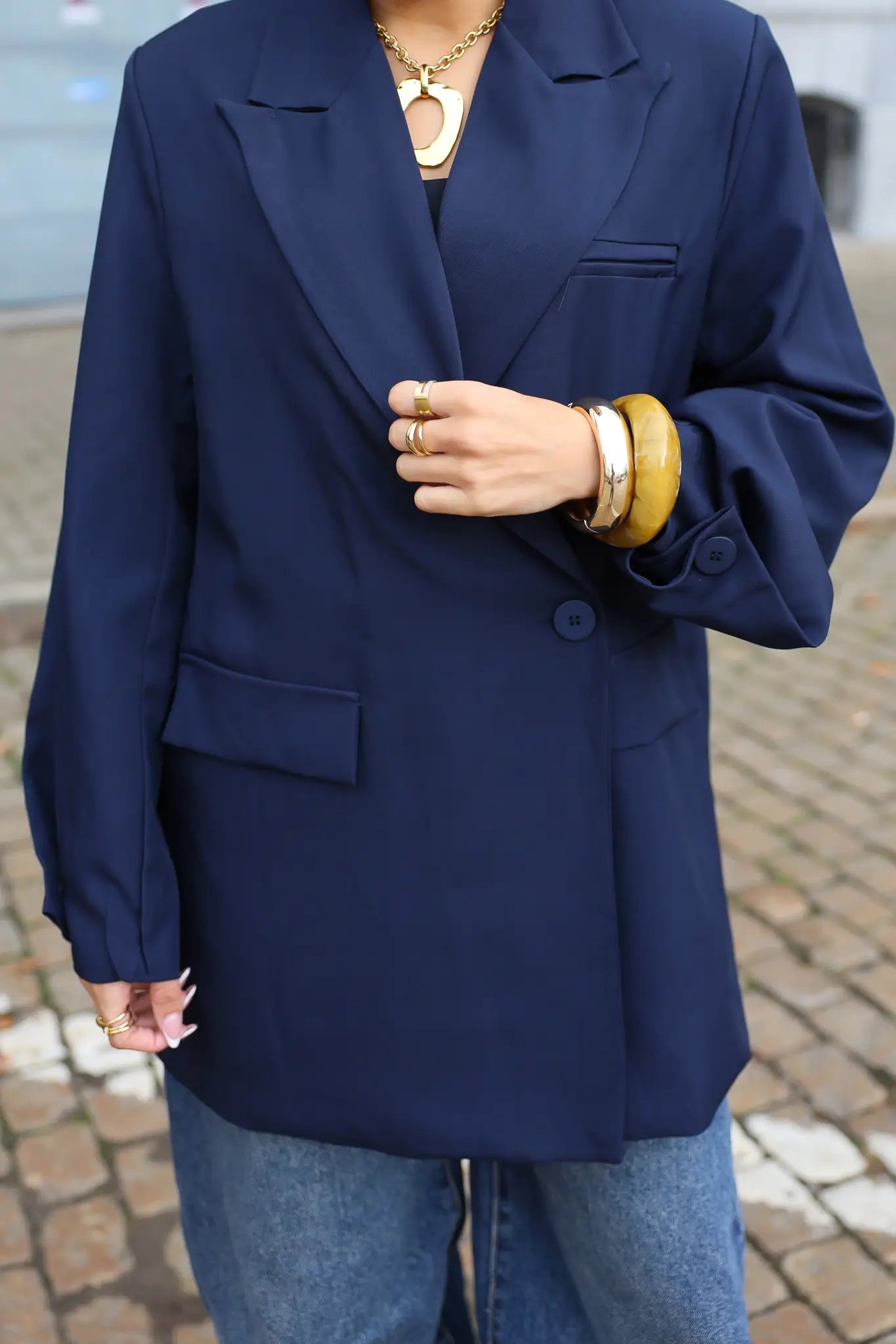 close up van donkerblauwe oversized blazer met zakken en gouden sieraden