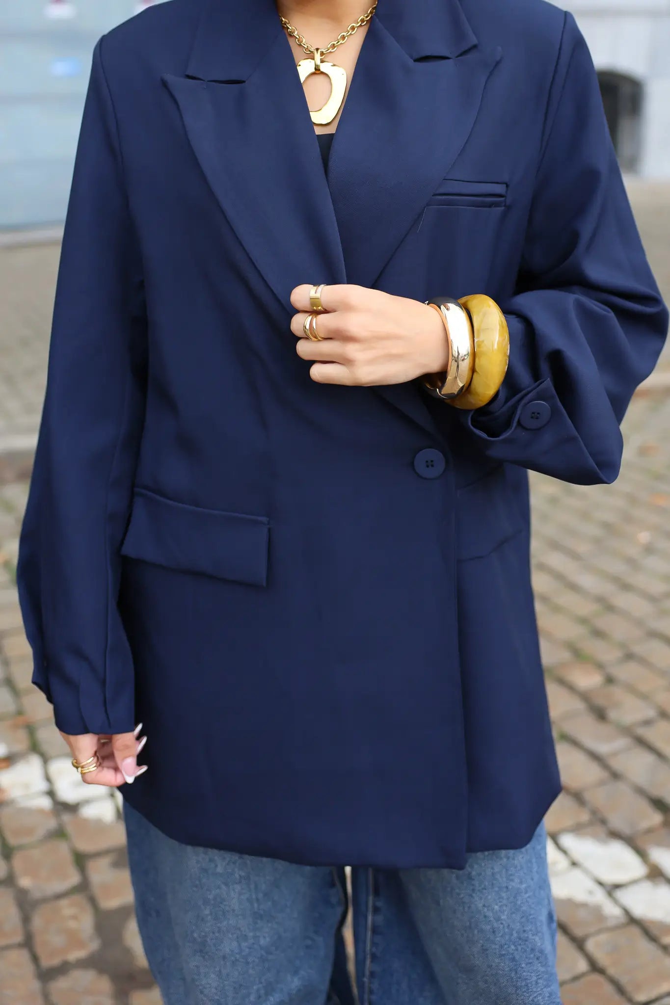 close up van donkerblauwe oversized blazer met zakken en gouden sieraden