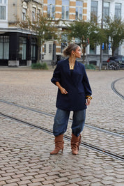 vrouw met donkerblauwe oversized blazer en laarzen kijkt opzij in straatbeeld