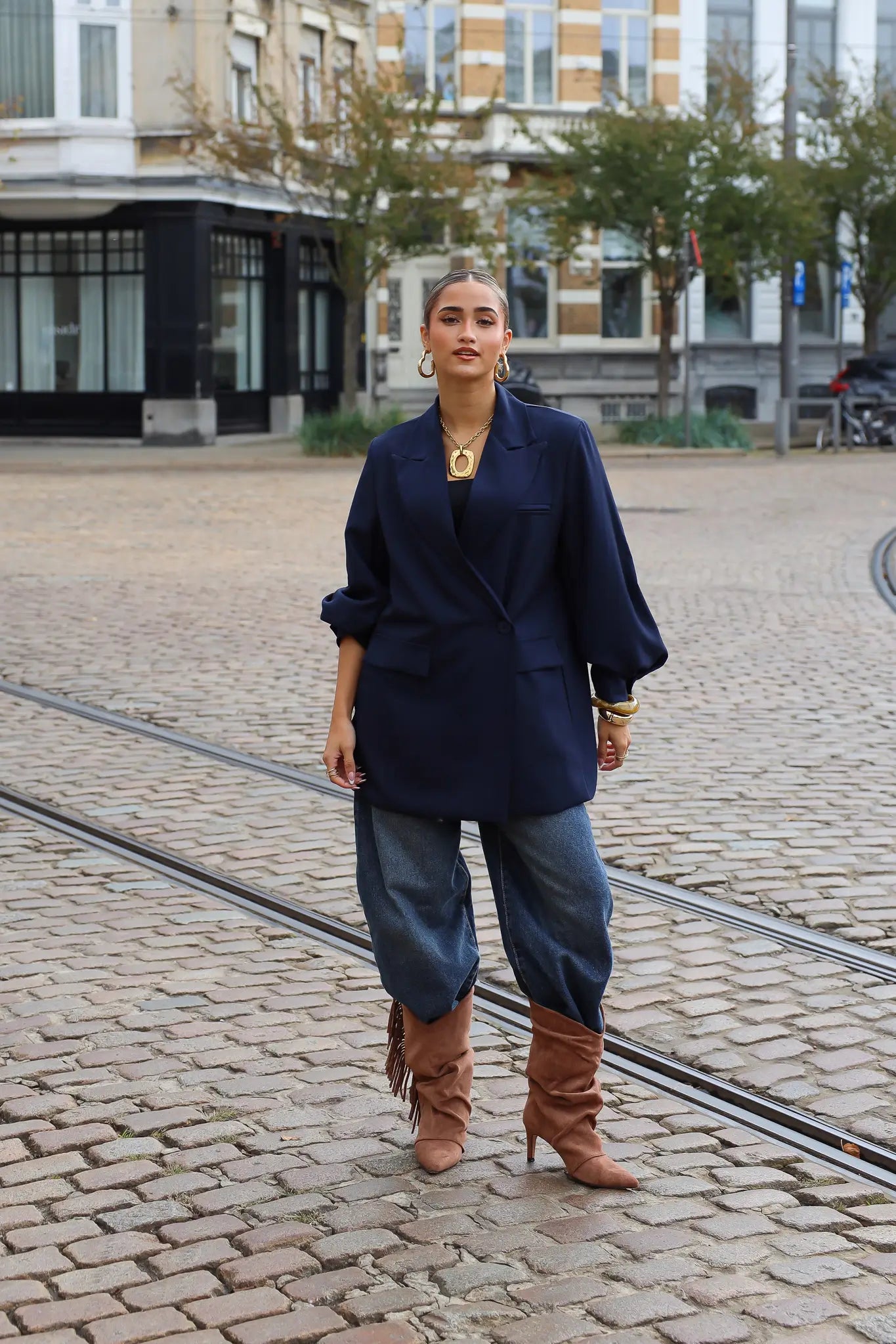 vrouw draagt donkerblauwe oversized blazer met jeans en bruine laarzen op straat