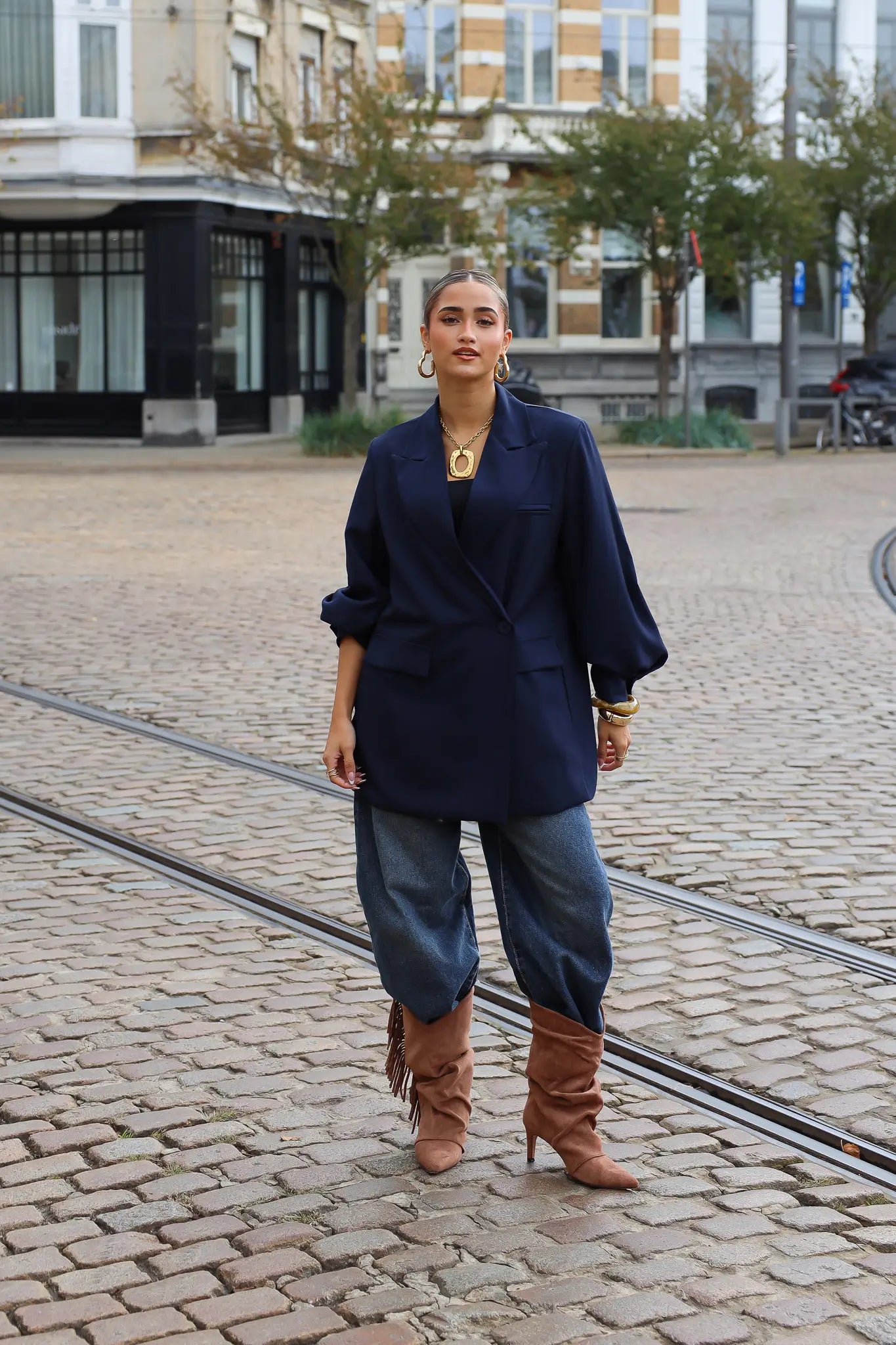 vrouw draagt donkerblauwe oversized blazer met jeans en bruine laarzen op straat