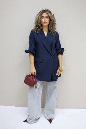 vrouw met donkerblauwe oversized blazer en rode handtas poseert tegen lichte muur