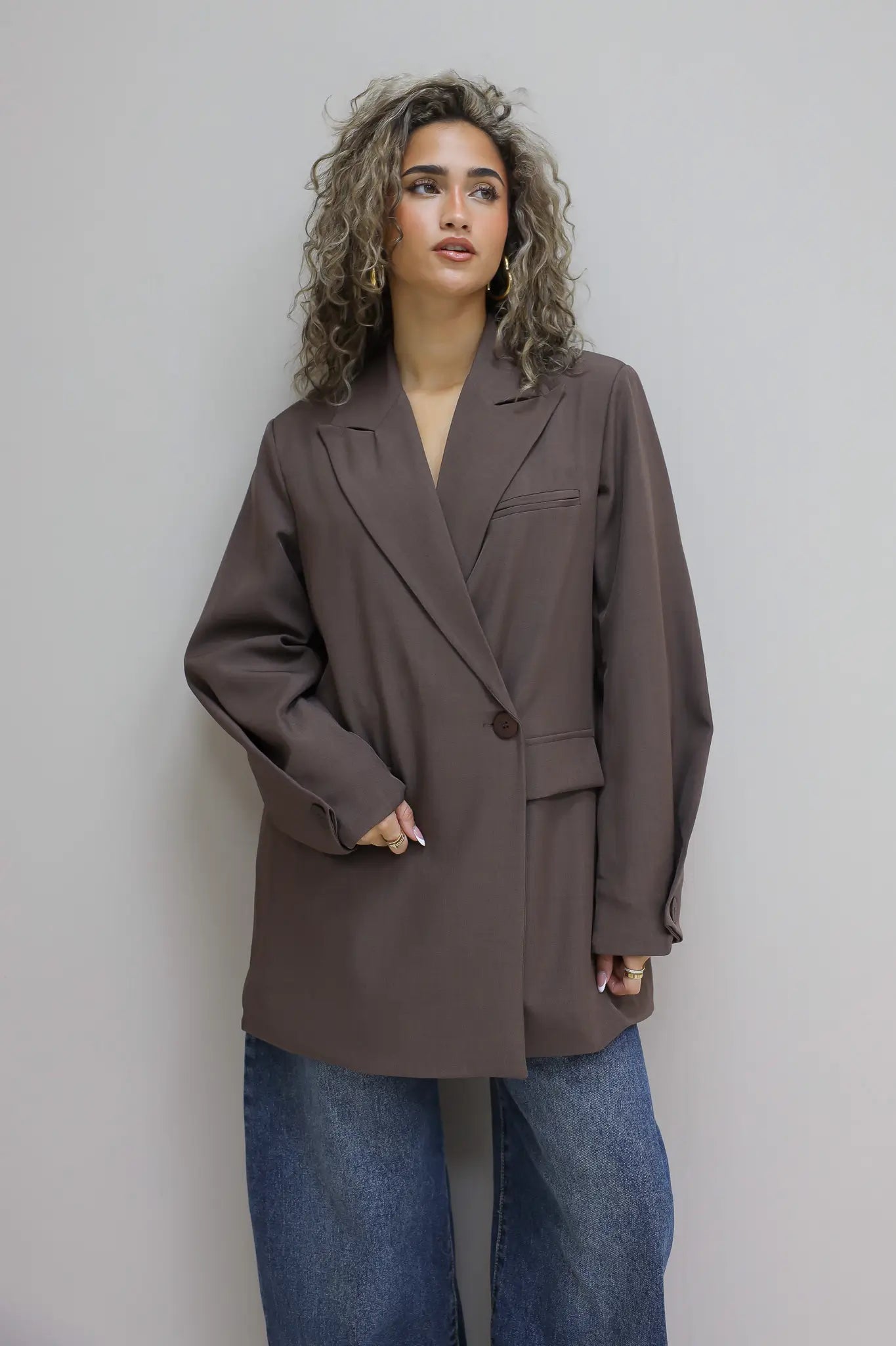 vrouw met donkerbruine oversized blazer en koffie in hand leunt tegen groene deur